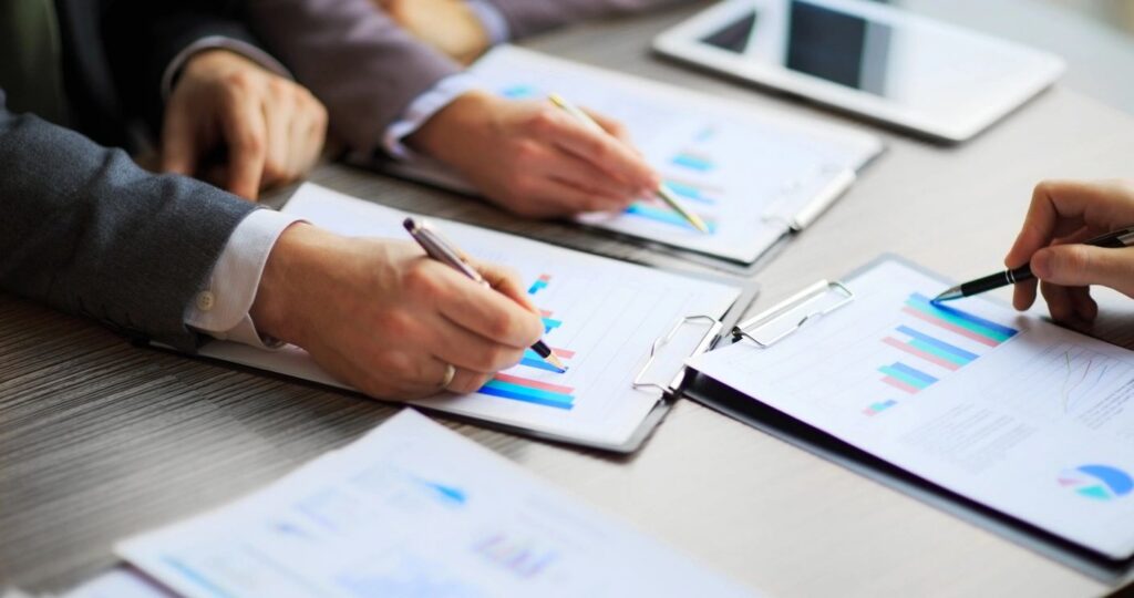 Hands reviewing and signing insurance readiness documentation with supporting charts, representing preparation of the paperwork carriers expect.